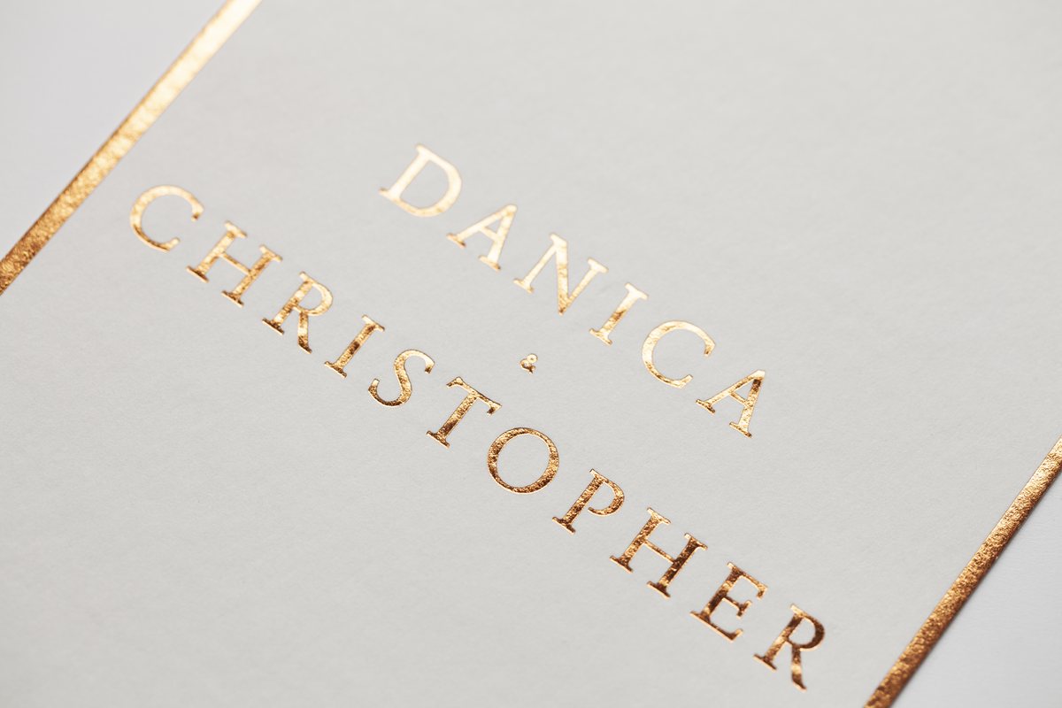 A pale card in close view shows foil stamping in rose gold capitals and a thin rose gold line along two edges.