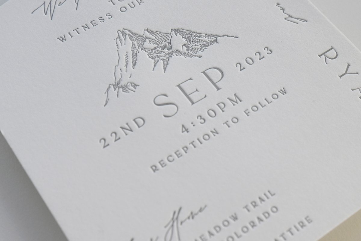 A close view of thick white cotton paper shows letterpress, with text and a mountain line drawing pressed into the paper.