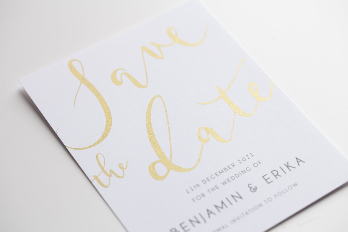 A white card at an angle shows metallic print in gold handwritten script and small dark capitals.
