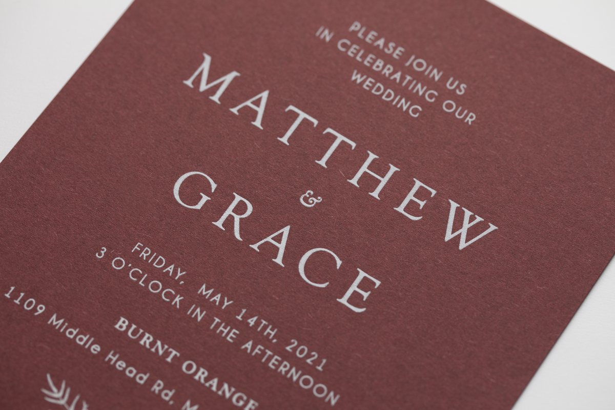 A burgundy card shows white ink in large serif capitals and smaller capitals, with visible paper texture.