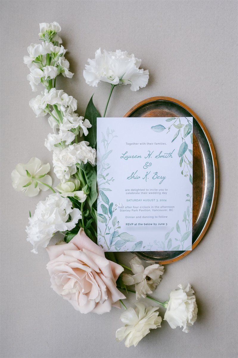 Botanical Geo wedding invitation with watercolour eucalyptus leaves and teal green names, styled with flowers on a copper tray